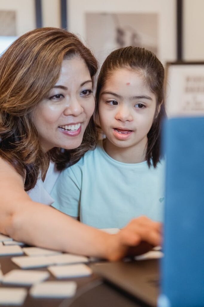 Betreuerin hilft einem Mädchen mit Down-Syndrom am Laptop